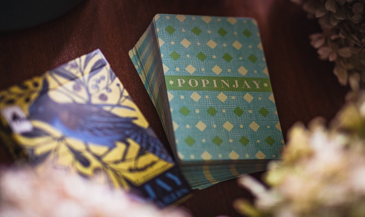 Two playing card decks, one with a blue and yellow design and the other with a green and white pattern, on a textured surface.
