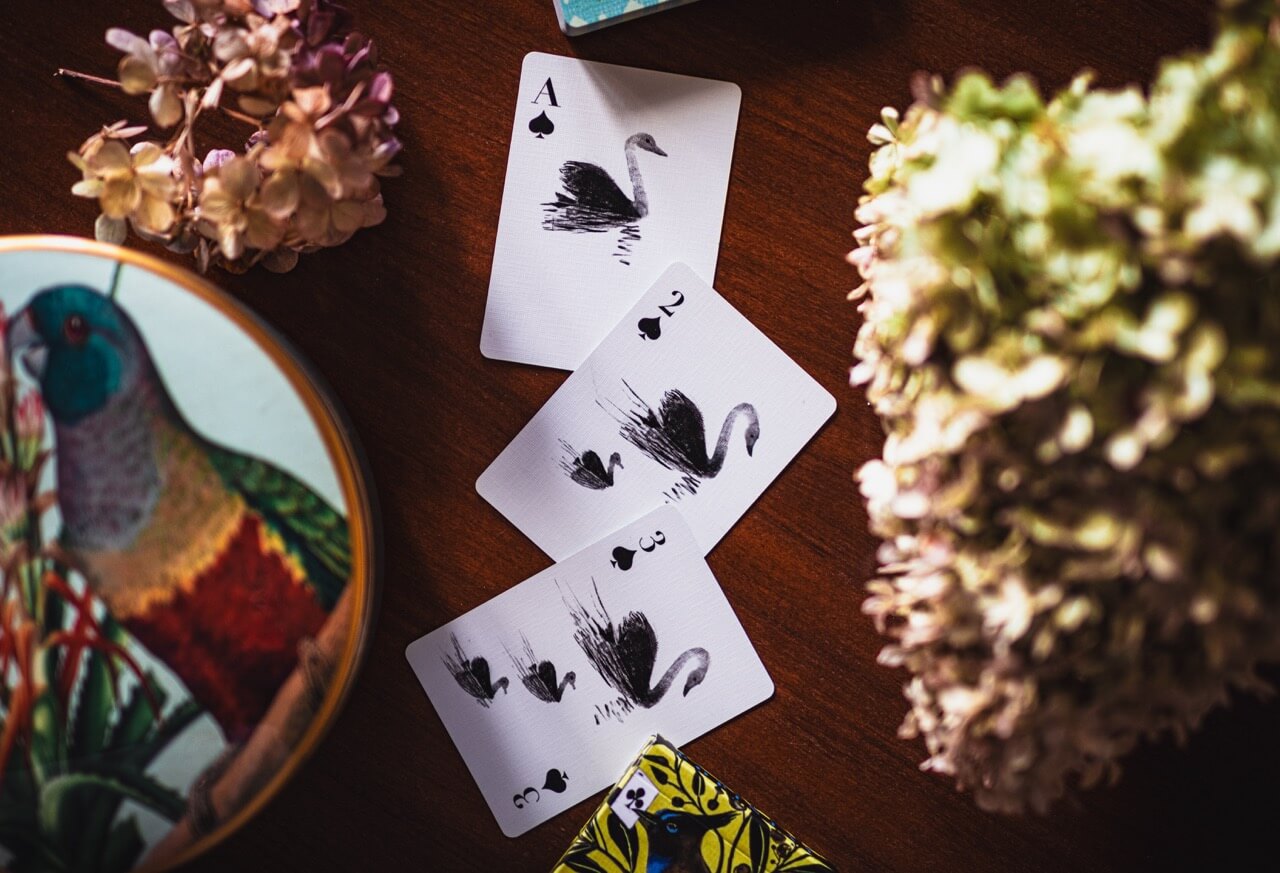 Playing cards with swan design on a wooden surface with decorative elements.