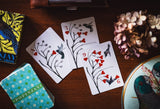 Playing cards with nature-themed design on a wooden surface, next to a box and decorative elements.