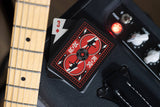 Guitar effects pedal with a deck of cards on top, next to a guitar neck.