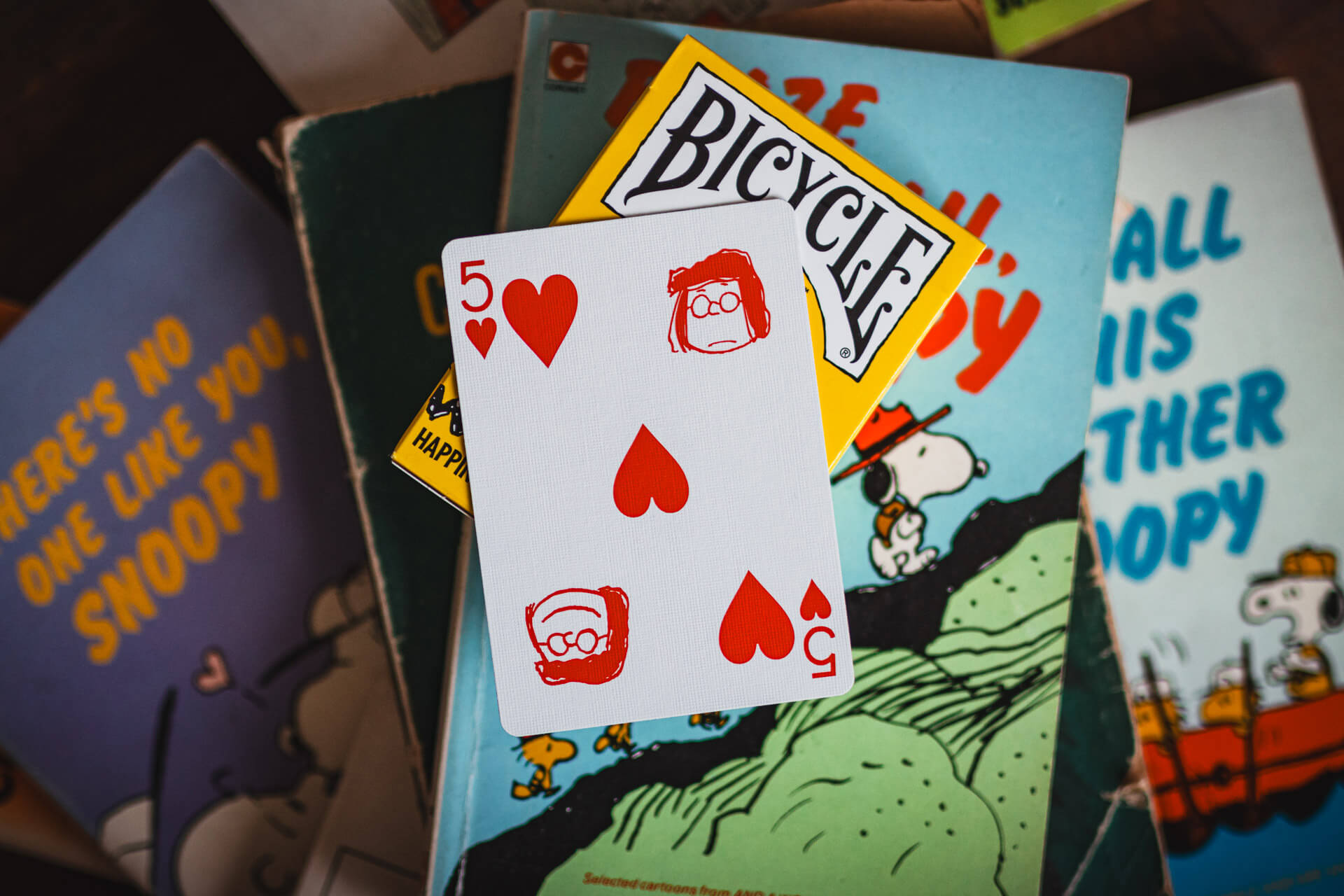 Playing card with hearts and 'Bicycle' logo on a Snoopy-themed book cover.