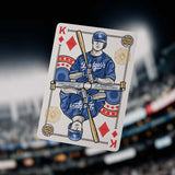 Playing card with a baseball player design, featuring the Los Angeles Dodgers logo, held in front of a stadium.